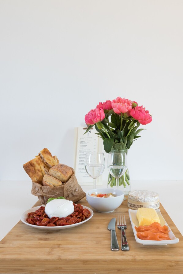 A wooden table with a plate of food, a bowl of olives, a glass of water, a vase of flowers, and a menu. - Penthouse with Terrace, Pantheon and 360° City views!! Walk to all attractions (Roma)