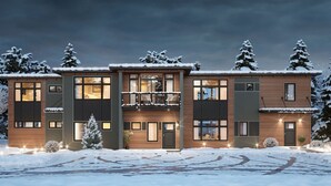 Een modern meerlaags gebouw met balkon, grote ramen en een besneeuwde omgeving.