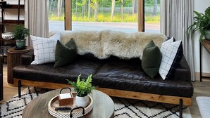 Een ruime woonkamer met een groot raam, een leren bank en een opgehangen herten schedel.