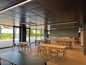 A modern interior with tables and chairs, a kitchen area, and large windows offering a view of the outdoors. - QVIST HOTEL (Dangjin)