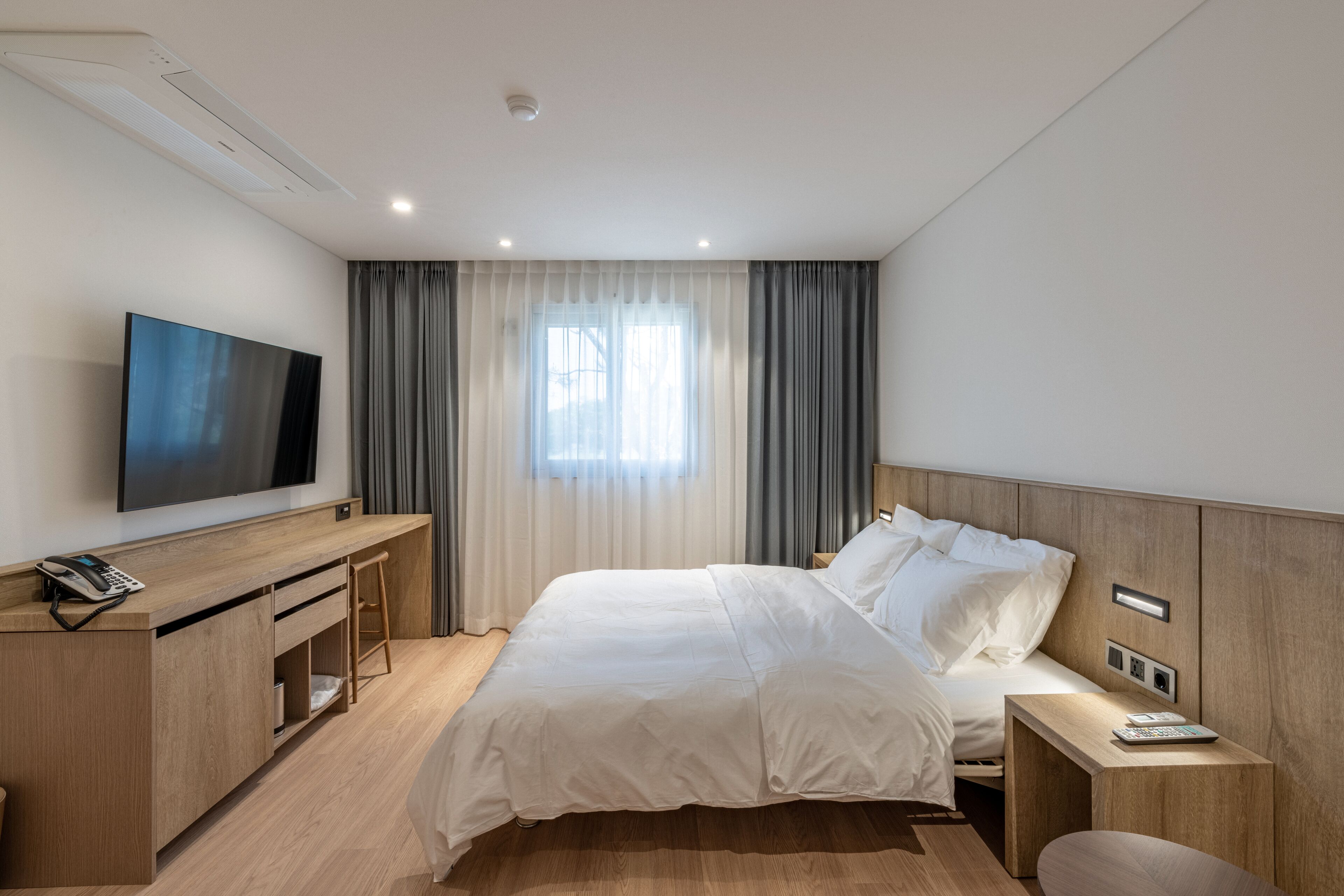 A modern hotel room with a large bed, a desk with a flat-screen TV, and a window with curtains.