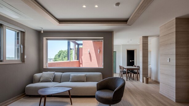 A modern living room with a sofa, a round table, and a chair. There is a large window providing a view of the outside. - QVIST HOTEL (Dangjin)