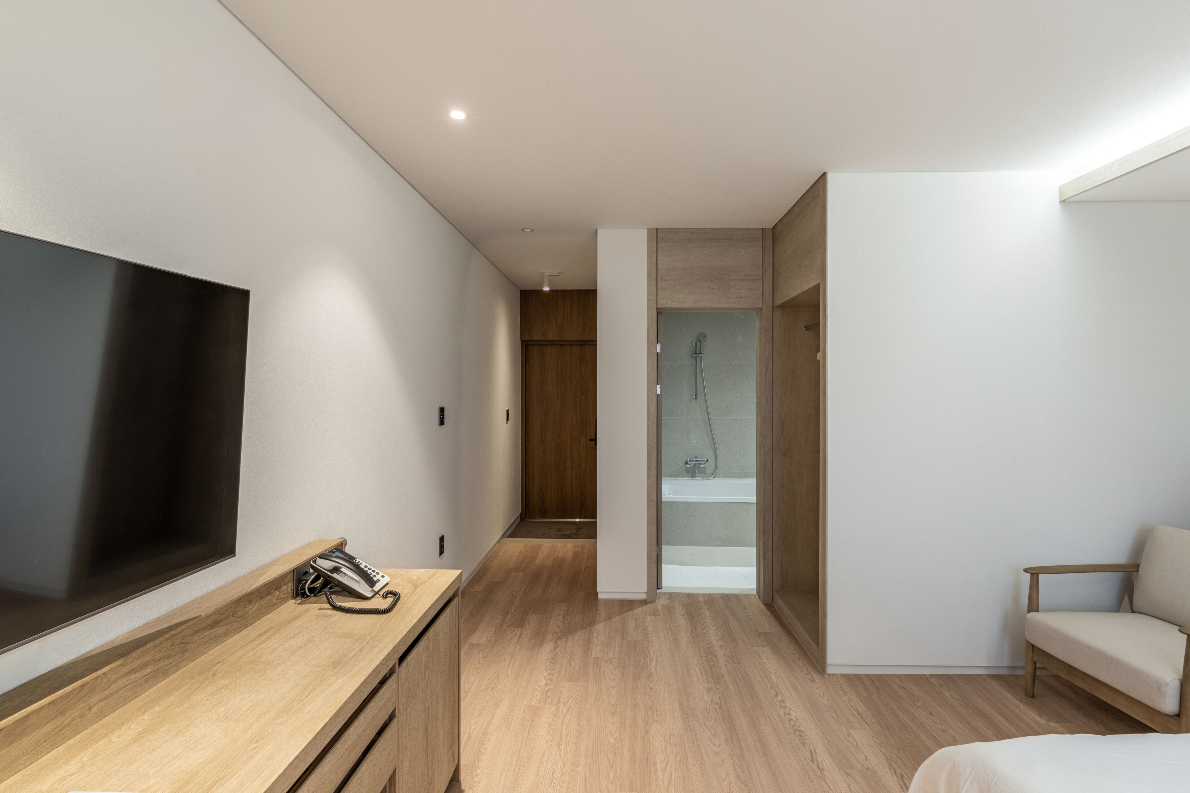 A modern hotel room with a large flat-screen TV, a wooden dresser, a bed, a sofa, and a shower area.