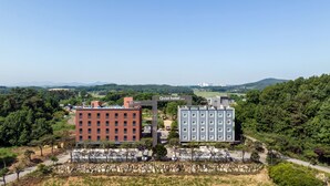 A hotel complex with two prominent buildings, one red and one blue, surrounded by greenery and a clear sky. - QVIST HOTEL (Dangjin)