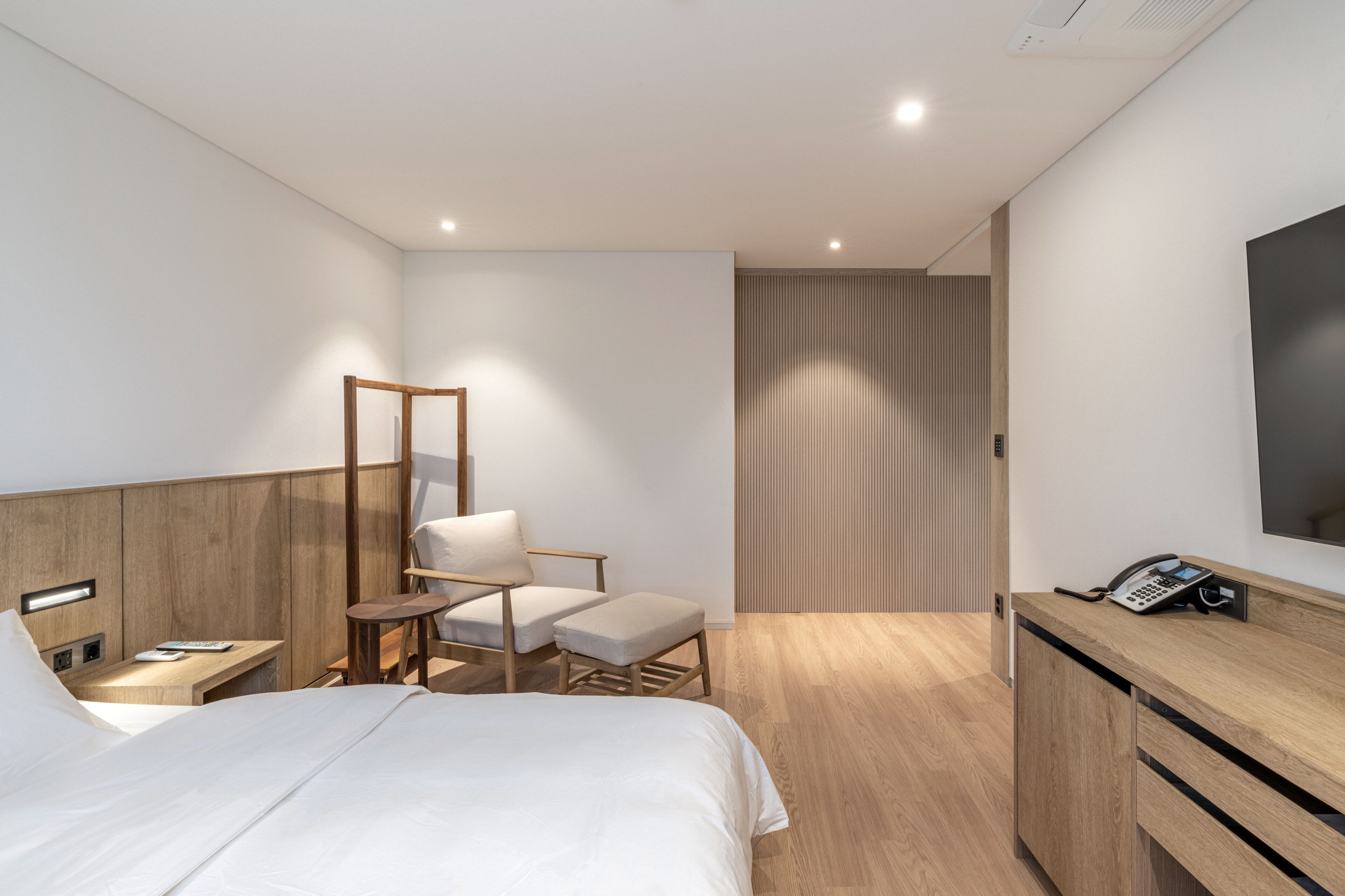 A modern hotel room with a bed, a desk, a chair, a mirror, a TV, and a phone.