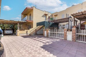 Un edificio residencial con entrada porticada, un coche aparcado fuera y una escalera que lleva al piso superior.