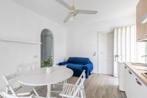 Une cuisine moderne avec des meubles blancs, une table à manger blanche avec des chaises, un ventilateur de plafond et un canapé bleu.