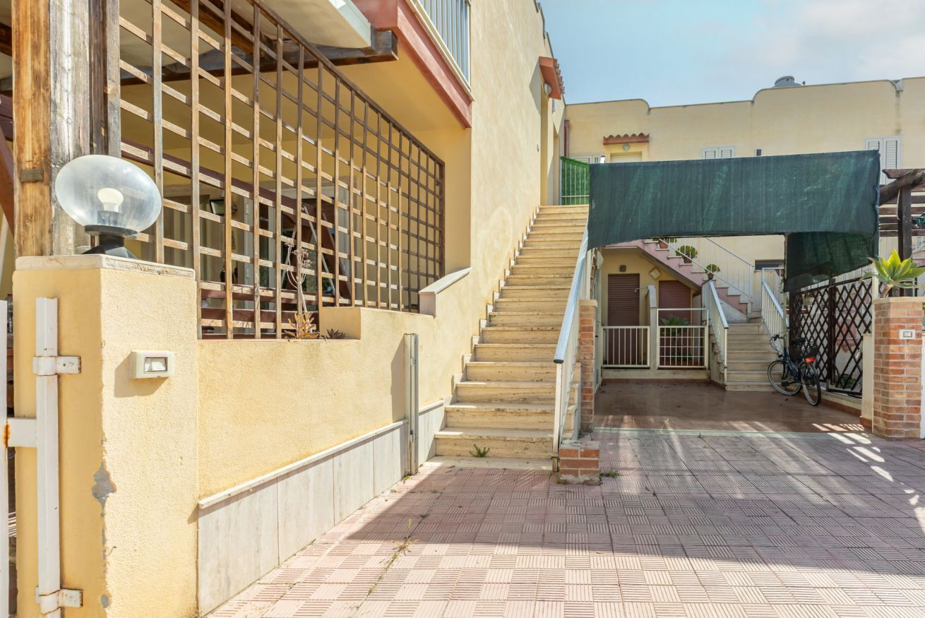 Un edificio residencial con una escalera que lleva al segundo piso, una antena parabólica y una entrada con portón.