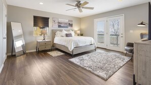 A bedroom with a bed, nightstands, a ceiling fan, a large window, and a view of the outdoors.