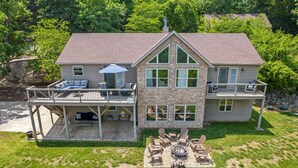 A two-story house with a stone facade, a covered patio with outdoor furniture, and a fire pit in the backyard.