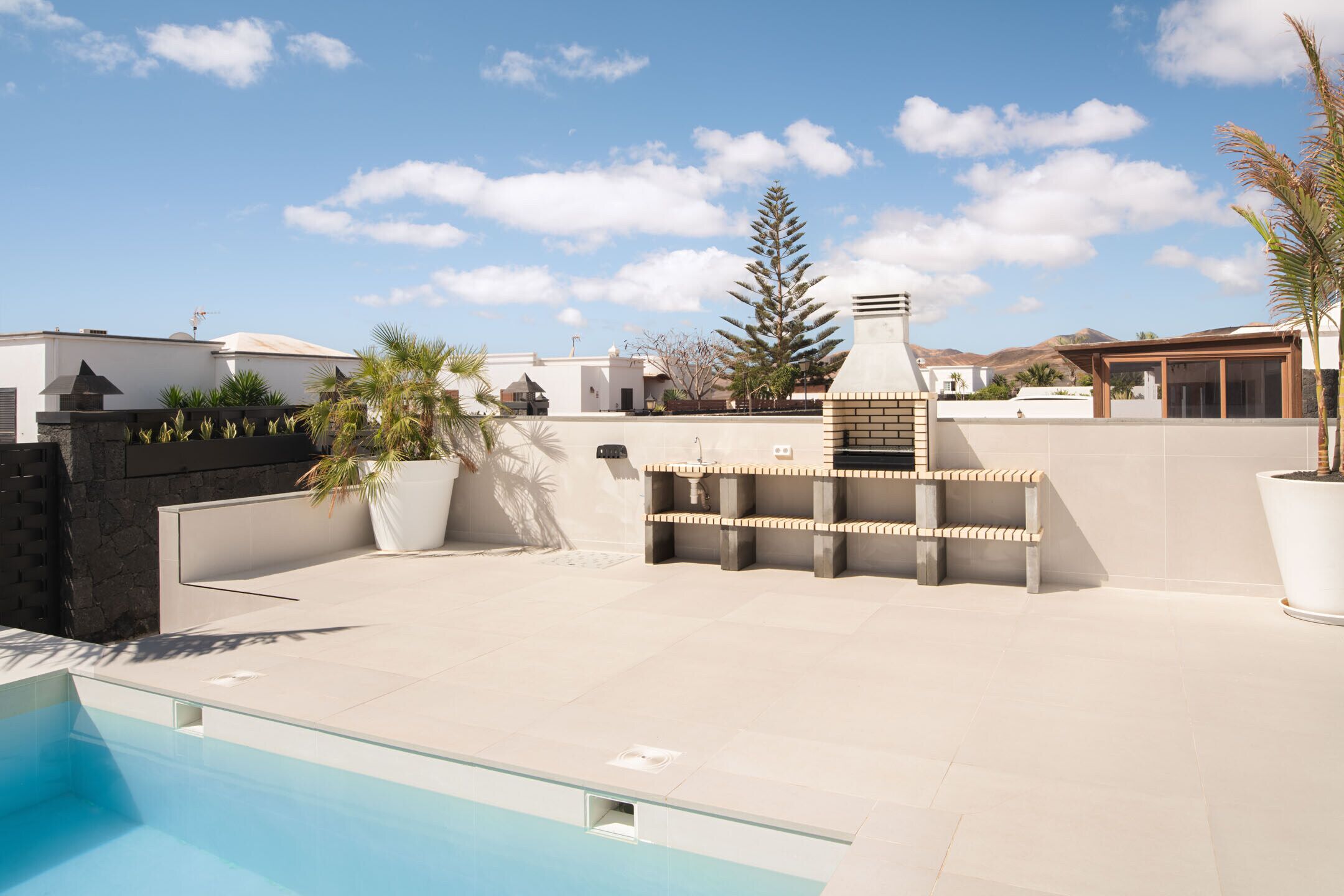 A rooftop pool area with a clear view of the sky, a barbecue setup, and a potted plant.
