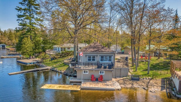 A lakeside property with a dock, a house with a balcony, and a small boat. - Barefoot Beach on Pigeon Lake  (Bobcaygeon)