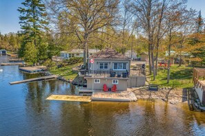 A lakeside property with a dock, a house with a balcony, and a small boat.