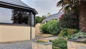 A modern house with a stone exterior, a gravel driveway, and a garden with various plants and flowers. - Ker Rosy - Saint Gildas DE Rhuys (SAINT GILDAS DE RHUYS)