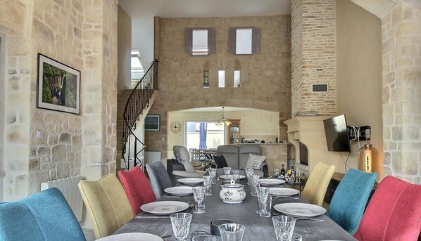 Un espace repas avec un mur en pierre, un escalier et une vue sur la cuisine.