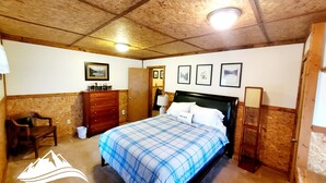 Ein Schlafzimmer mit Bett, Kommode, Stuhl und gerahmten Bildern an der Wand.