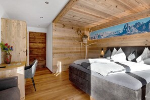 Une chambre avec un plafond en bois, un lit avec une literie blanche, un bureau avec une chaise et un tableau représentant des montagnes.