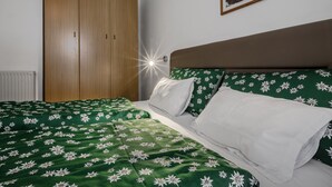 Ein Schlafzimmer mit einem Bett, floralem Bettbezug in Grün, einem Holzschrank und einem gerahmten Bild an der Wand.
