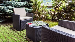 Outdoor wicker furniture with cushions, a magazine on a table, and a garden with trees and grass.