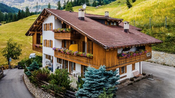 A chalet with a balcony, a stone wall, and a mountain view.