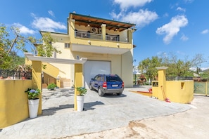 A two-story house with a car parked in the driveway, a garage door, and potted plants.