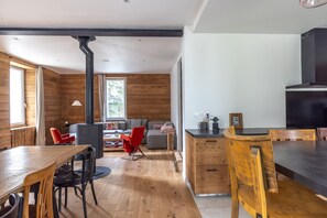Un intérieur moderne avec un plancher en bois, un coin repas avec une table et des chaises, une cuisine équipée d’une cuisinière et un salon avec un canapé et des fauteuils rouges.