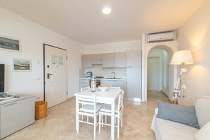A modern living room with a white sofa, a dining table with chairs, a TV, and a kitchen area with cabinets and a sink.