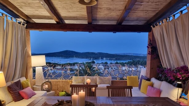 A terrace with a table set for dining, candles, and a view of the sea and hills. - Apartment 'Il Fiordo 28' with Sea View, Shared Pool and Air Conditioning (Santa Teresa Gallura)