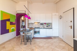 Une cuisine compacte avec des meubles blancs, une cuisinière en acier inoxydable et un tabouret de bar.