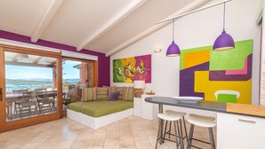 A modern kitchen with a dining area, a colorful abstract painting, and a view through the glass door. - Apartment 'Il Fiordo 28' with Sea View, Shared Pool and Air Conditioning (Santa Teresa Gallura)