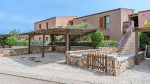 A courtyard with stone walls, a pergola, and a staircase leading to a building with a tiled roof. - Apartment 'Il Fiordo 28' with Sea View, Shared Pool and Air Conditioning (Santa Teresa Gallura)