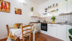 A kitchen with white cabinets, a tiled backsplash, a dining table with chairs, and a fruit basket.
