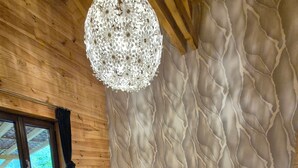 Une chambre avec un plafond en bois, un grand lustre, un lit recouvert d’une literie à motifs floraux et une fenêtre avec des rideaux.