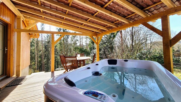 Une terrasse en bois avec un jacuzzi, une table et des chaises, le tout installé sous une pergola.