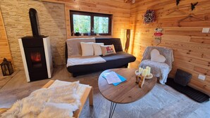 L’intérieur d’un chalet accueillant, avec un mur en pierre, une cheminée, un canapé, un fauteuil et une petite table décorée de bougies.