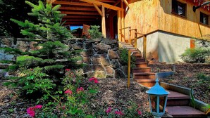 Un bâtiment en bois doté d’un escalier en pierre, entouré de verdure et de fleurs.