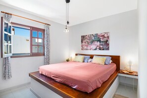 Een slaapkamer met een bed, een raam met gordijnen, een wandlamp en een schilderij.