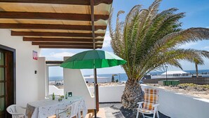 Um alpendre coberto com mesa, cadeiras e um guarda-sol verde.