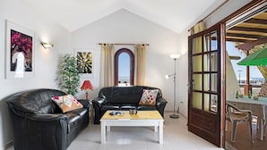 Uma sala de estar com um sofá de couro preto, uma mesa de centro branca e uma área de jantar com mesa e cadeiras.