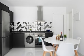 Een moderne keuken met een wasmachine, oven en een eethoek met stoelen en een tafel.