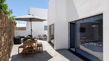A modern outdoor patio with a table, chairs, and a large umbrella.