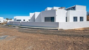 Um edifício moderno branco com telhado plano, janelas amplas e piso pavimentado.