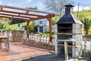 An outdoor patio with a stone barbecue grill, a wooden pergola, and a dining table.