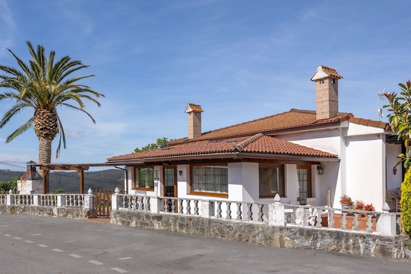 A two-story building with a tiled roof, a stone wall, and a palm tree in the foreground.
