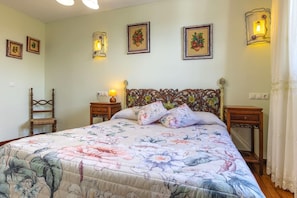A bedroom with a floral bedspread, a wooden headboard, two bedside tables with lamps, and framed artwork on the walls.
