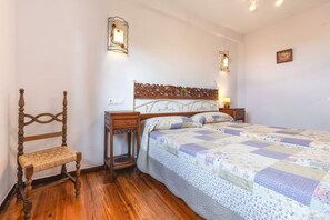 A bedroom with a wooden bed, a bedside table, a chair, and two wall-mounted light fixtures.