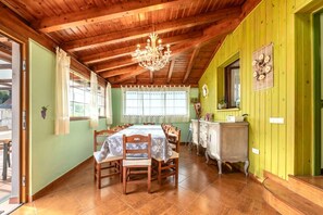 A dining area with a wooden table and chairs, a chandelier, and a green wall. - Holiday Home 'Casa Rural La Praderia' with Mountain Views, Private Terrace and Wi-Fi (Vidular)
