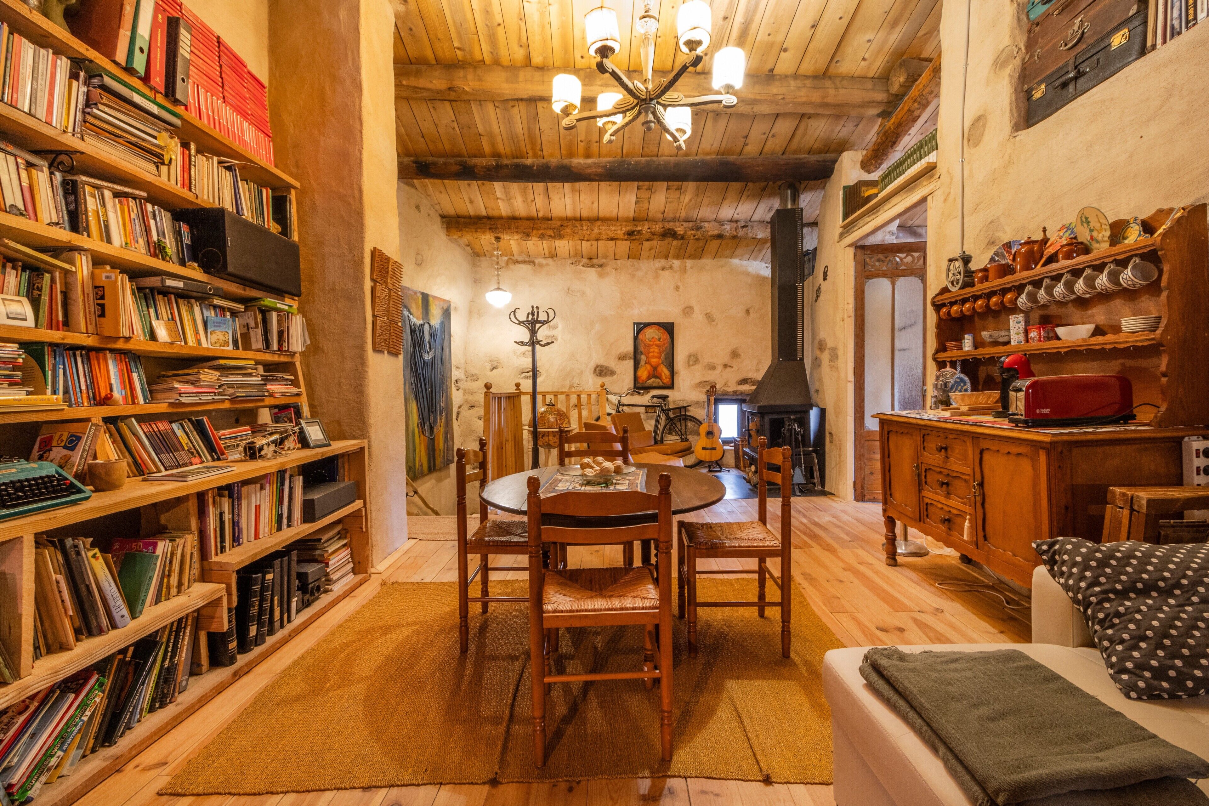 Una habitación acogedora con techo de madera, una mesa de comedor con sillas, una estantería y una chimenea.