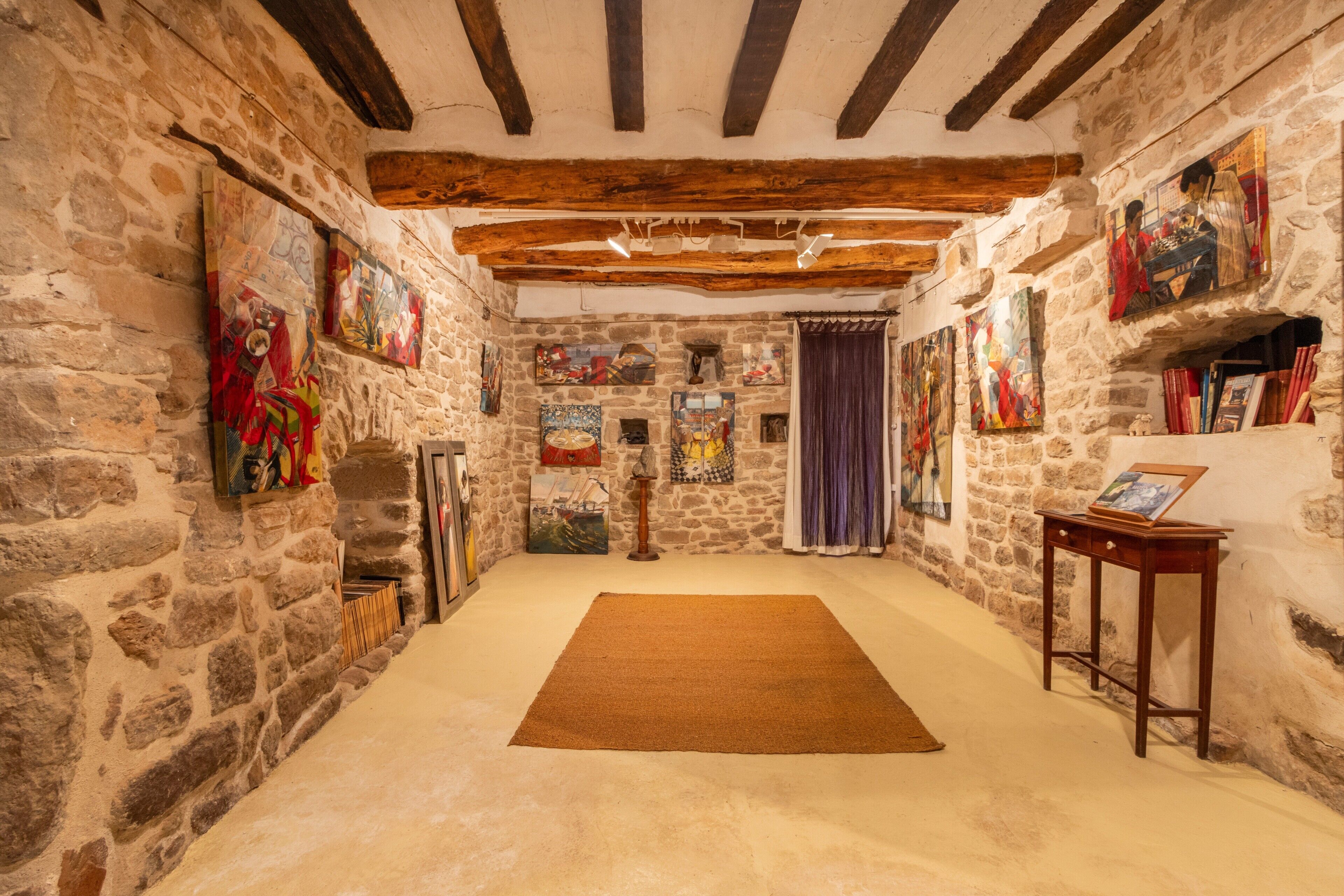 Une pièce aux murs de pierre, avec un plafond en bois, un tapis marron et diverses œuvres d’art accrochées aux murs.