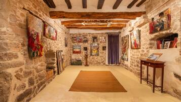 Une pièce aux murs de pierre, avec un plafond en bois, un tapis marron et diverses œuvres d’art accrochées aux murs.